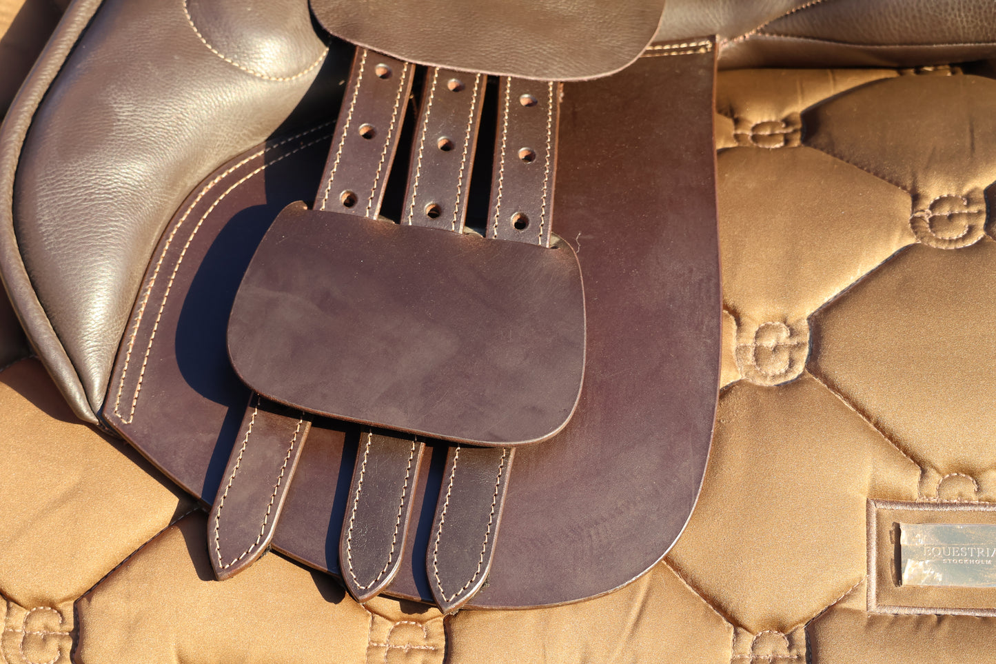 Close-up of a brown leather saddle pad on a beige quilted surface.