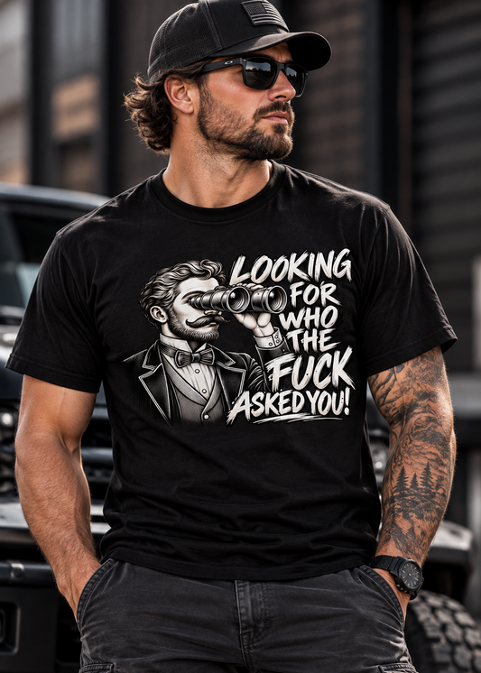 A man wearing a black graphic t-shirt with a white print of a man with binoculars and the text 'LOOKING FOR WHO THE FUCK ASKED YOU!' in a street setting.