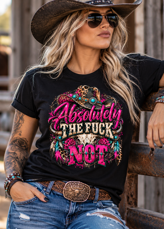 A woman wearing a black graphic t-shirt with a colorful western-themed design that reads 'Absolutely THE FUCK NOT', paired with a cowboy hat, sunglasses, and jeans, leaning on a rustic wooden fence.